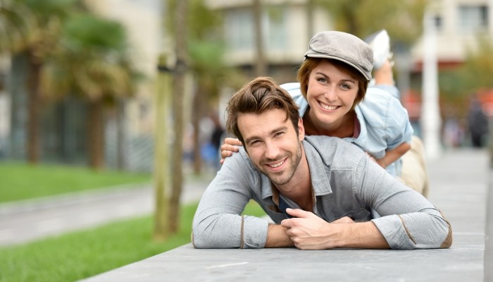 Smiling man and woman laying on their stomachs on concrete outdoors