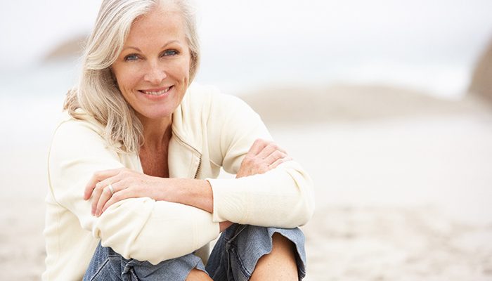 Senior woman smiling and sitting at the beach