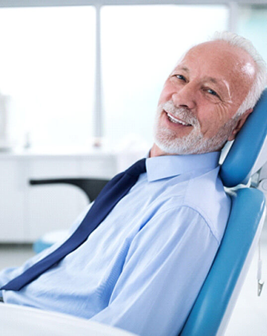 senior man leaning back in dental chair and smiling