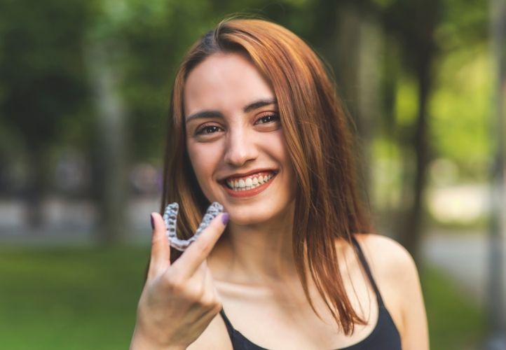 Smiling woman outdoors holding Invisalign in Saint Peters