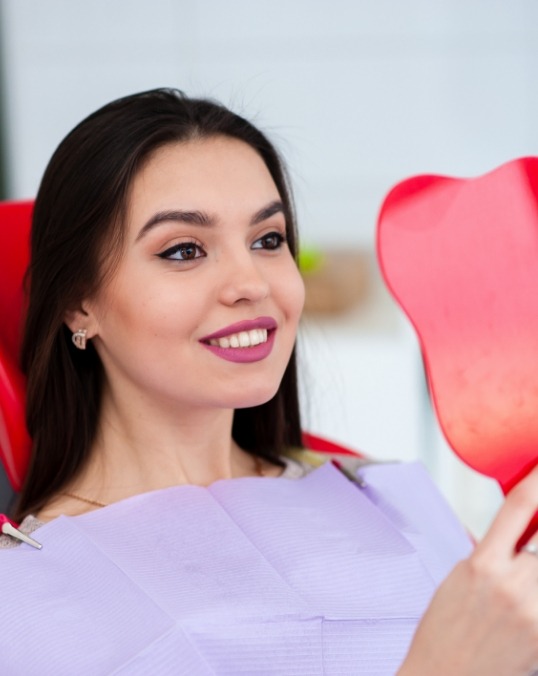 Young woman in dental chair seeing her teeth in a red mirror