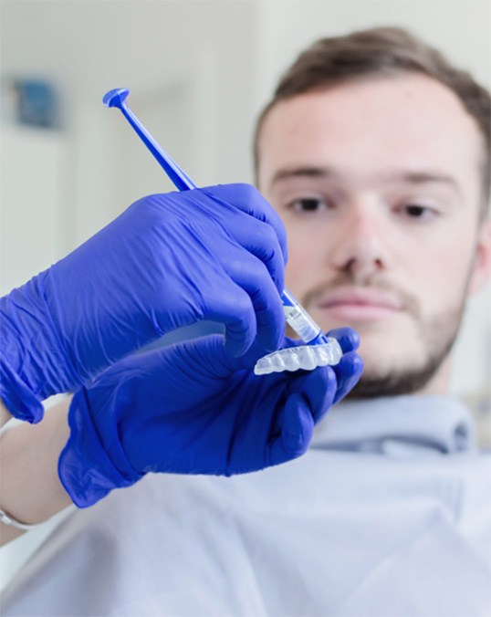 Man with brown hair in dental chair while tech prepares whitening kit