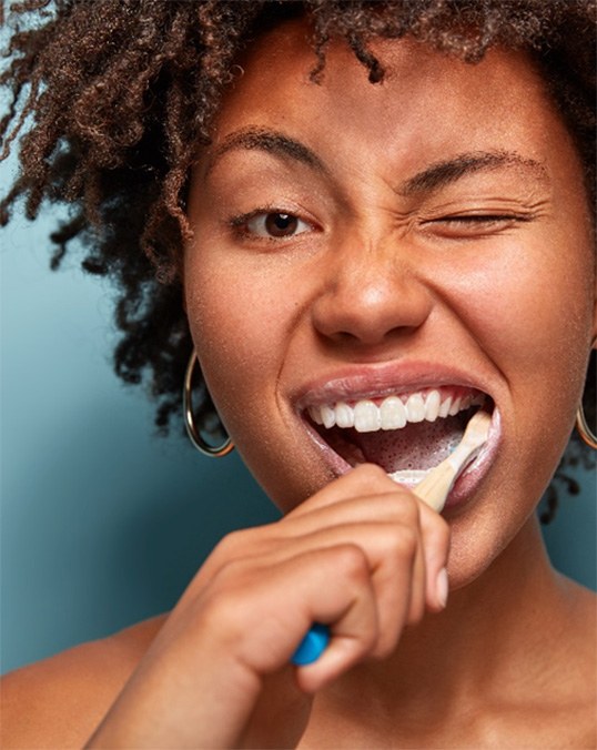 Woman with brown hair winking while brushing her teeth